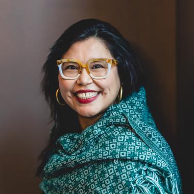 Rosa is wearing blue and yellow glasses, she is smiling and has a green patterned rebozo wrapped around her shoulders.